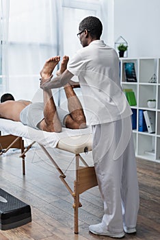 african american rehabilitologist stretching legs of
