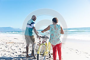 African american retired senior couple with bicycles at beach on sunny day