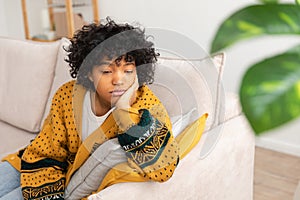 African american sad thoughtful pensive unmotivated girl sitting on sofa at home indoor. Young african woman ponder look