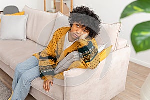 African american sad thoughtful pensive unmotivated girl sitting on sofa at home indoor. Young african woman ponder look