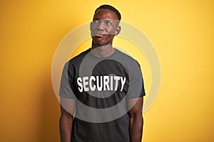 African american safeguard man wearing security uniform over isolated yellow background smiling looking to the side and staring