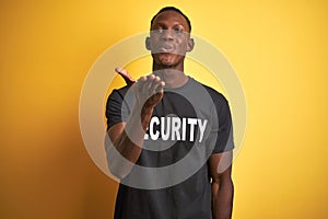 African american safeguard man wearing security uniform over  yellow background looking at the camera blowing a kiss with