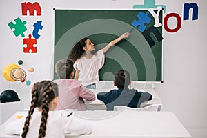 African american schoolgirl pointing at chalkboard while classmates studying at desks