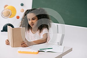 African american schoolgirl reading textbook in class