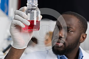 African American Scientist Examine Flask With Red Luquid Working In Modern Laboratory, Male Researcher Making Experiment