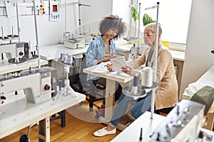 African-American seamstress with mature colleague work together in light studio