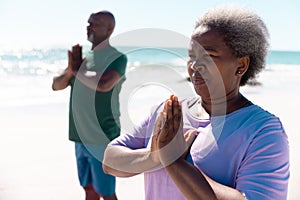 African american senior couple meditating at beach against clear sky during summer