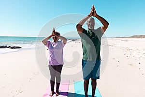 African american senior couple meditating in mountain pose at beach against clear sky