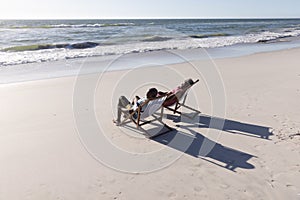 African american senior couple sitting on deckchairs in front of seascape at beach during summer