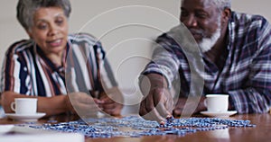 African american senior couple sitting by table doing puzzles drinking tea