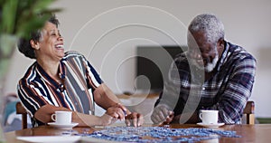 African american senior couple sitting by table doing puzzles drinking tea