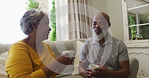 African american senior couple smiling while having coffee together sitting on the couch at home