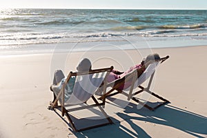 African american senior couple talking while sitting on deckchairs in front of seascape at beach