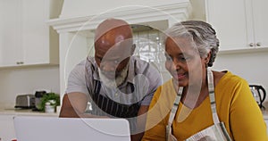 African american senior couple wearing aprons having a video call on laptop in the kitchen at home