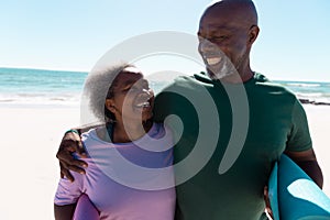 African american senior couple with yoga mats looking at each other against sea and clear sky