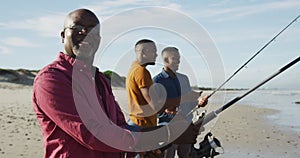 African american senior father and twin teenage sons standing on a beach fishing and talking