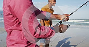 African american senior father and twin teenage sons standing on a beach fishing and talking