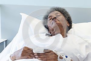 African american senior female patient sleeping in bed in sunny hospital room