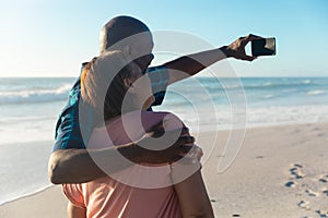 African american senior man with arm around woman taking selfie through smartphone at beach