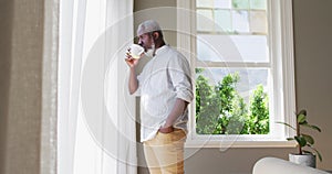 African american senior man drinking coffee while looking out of the window at home