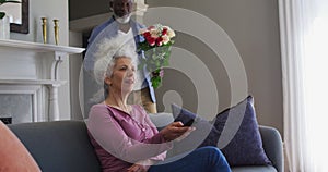 African american senior man giving flower bouquet to his wife at home