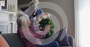 African american senior man giving gift box and flower bouquet to his wife at home