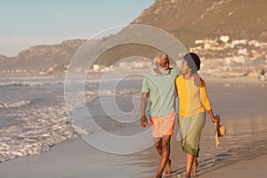 African american senior man with hand on mature woman\'s shoulder walking at beach at sunset