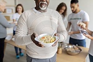 African american senior man holding plate with meal, receiving food in charity organization office, cropped, closeup
