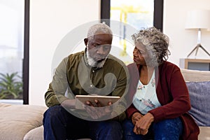 African american senior man using digital tablet while sitting with woman on sofa in nursing home