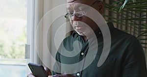 African american senior man using smartphone near the window at home