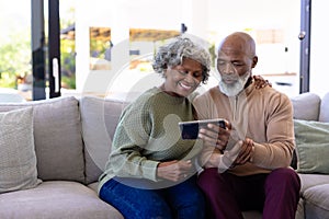 African american senior man with woman watching video over digital tablet on sofa in nursing home