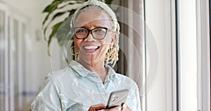 An African American senior woman beams with joy, holding a smartphone at home