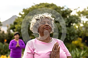 African american senior woman with eyes closed meditating against trees in yard at nursing home