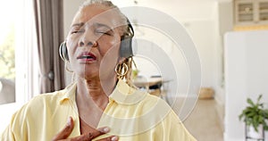 An African American senior woman mediating and wearing headphones with closed eyes at home