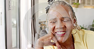 An African American senior woman is smiling broadly, resting her chin on her hand