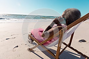 African american senior woman talking over mobile phone while relaxing on deckchair at beach