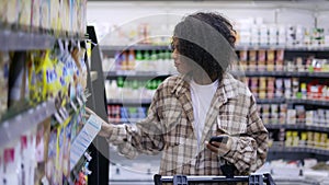 African American with shopping cart using smartphone at supermarket, slow motion