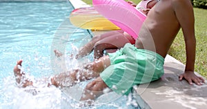 African American siblings splash water by a poolside at home, with a pink float nearby