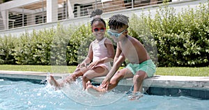 African American sister and brother enjoy poolside fun at home, splashing water with their feet