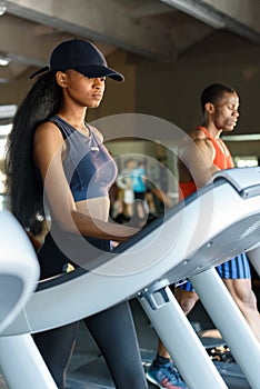 african american slim woman with her black handsome athletic trainer on the treadmill in gym. Fitness concept