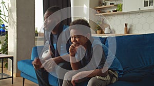 African American son and dad watching football game on tv, celebrating goal