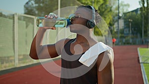 African American sport man in headphones listen music tired thirsty athlete runner drinking water healthy morning