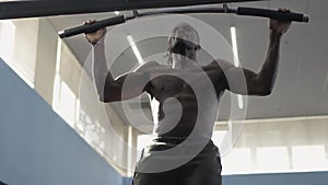 African American sportsman doing pull-ups with sunlight shining on muscular body. Medium shot of strong motivated
