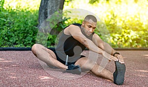 African American sportsman stretching his legs on jogging track at park