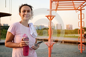 African American sportswoman with bottle of water and smartphone on the sportsground