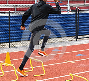 African American sprinter perfoming speed drills over yellow mini hurdles on a track