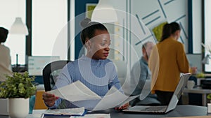 African american startup employee holding business papers with charts looking at laptop screen