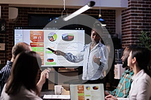 African american startup employee holding remote control presenting sales pie charts on tv screen