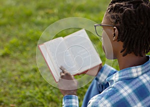 African American student guy reading outdoors sitting with opened book