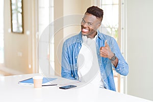 African american student man studying using notebooks and wearing headphones doing happy thumbs up gesture with hand